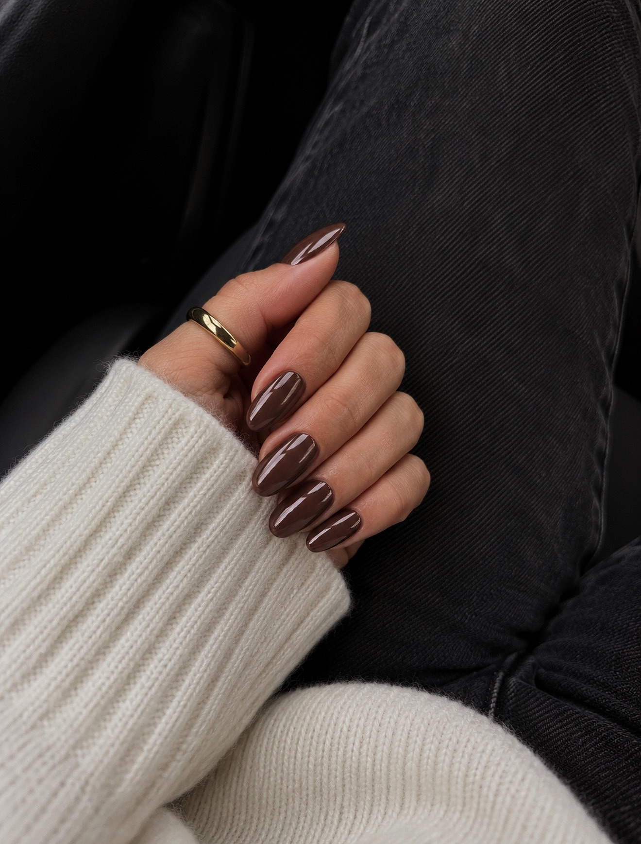 Glossy deep brown almond nails worn with a cream jumper